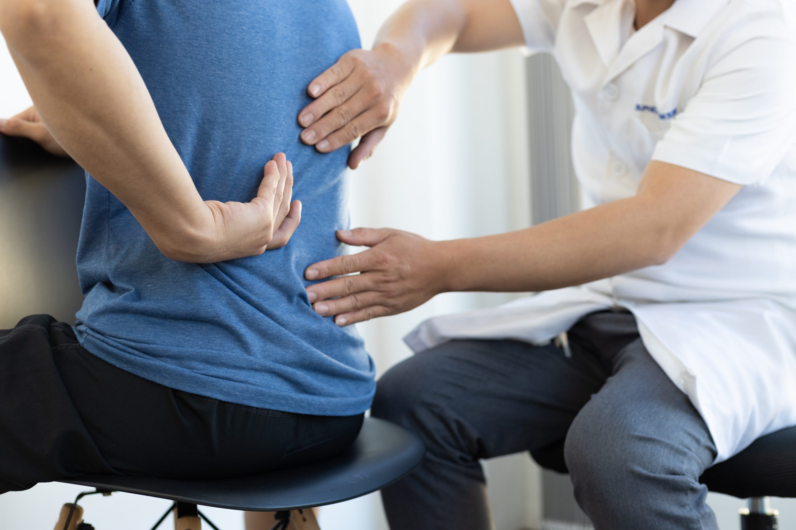 Healthcare practitioner assessing a patient's lower back during an in-clinic examination for back pain and mobility concerns.