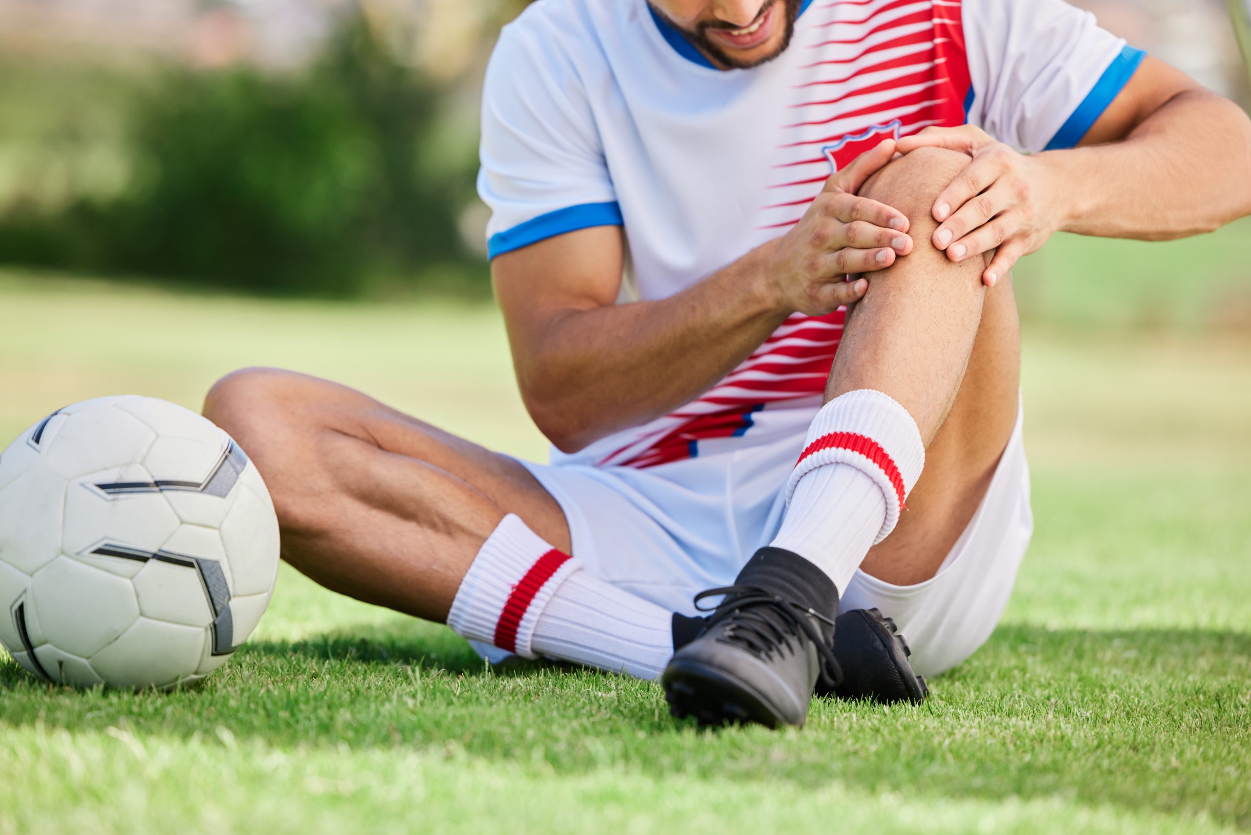 Soccer player sitting on the field holding an injured knee after a sports-related injury during a match.